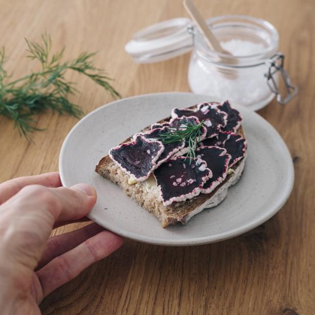 Eine Hand hält einen Teller mit einem Roggenbrot belegt mit Rote Bete und Dill.