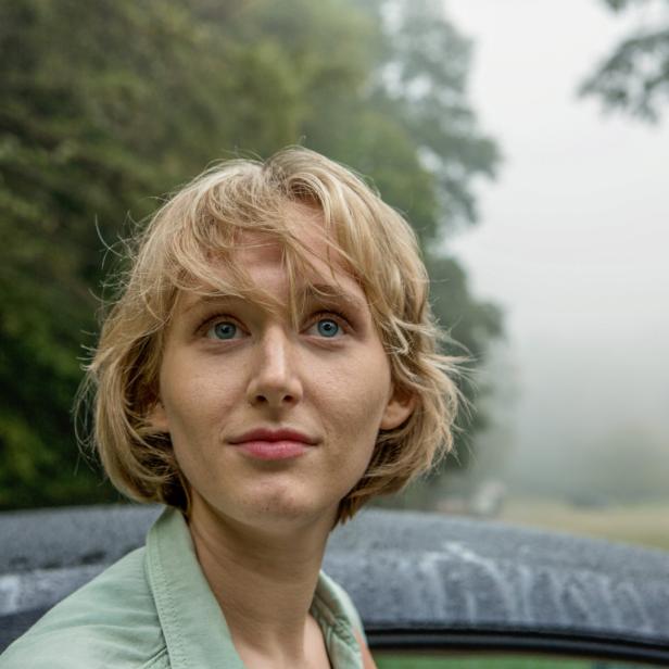 Eine junge Frau mit blonden Haaren und blauen Augen blickt nach oben.