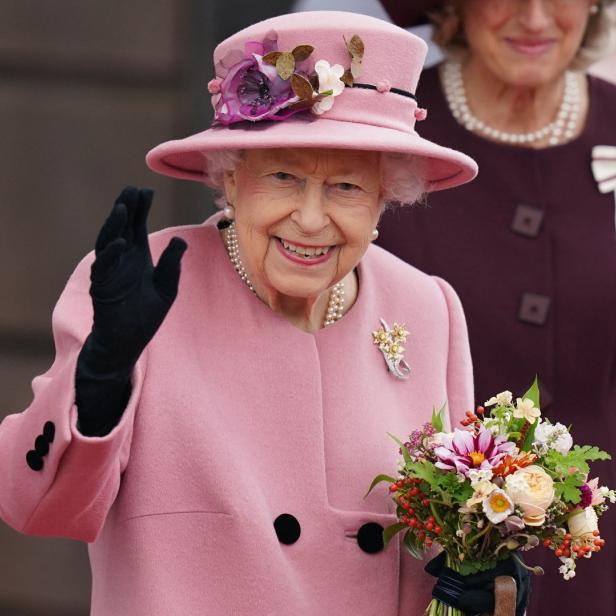 Königin Elisabeth II. lächelt, winkt und hält einen Blumenstrauß.