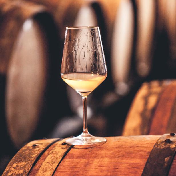 Ein Glas Weißwein steht auf einem Holzfass.