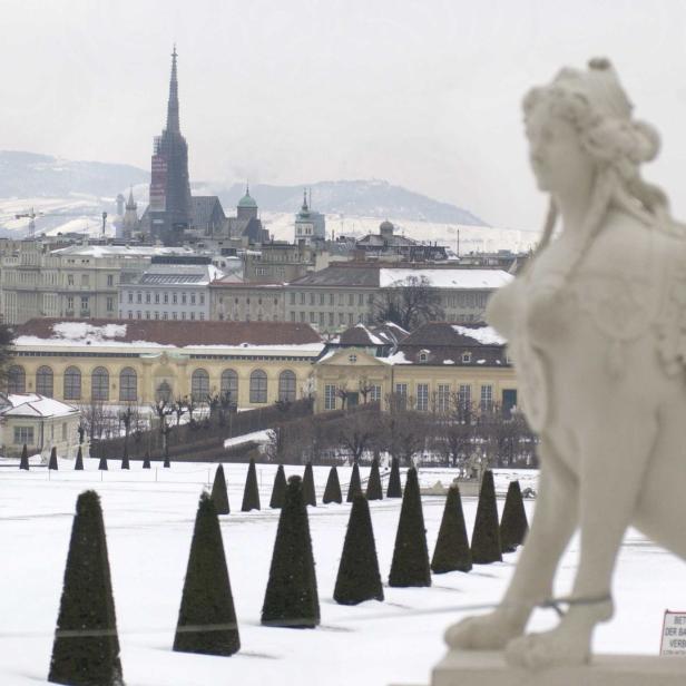 Blick über einen verschneiten Park auf Wien mit einer Sphinx-Statue im Vordergrund.
