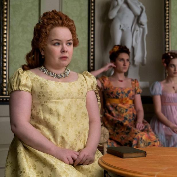 Penelope Featherington sitzt mit zwei anderen Frauen in einem eleganten Raum.