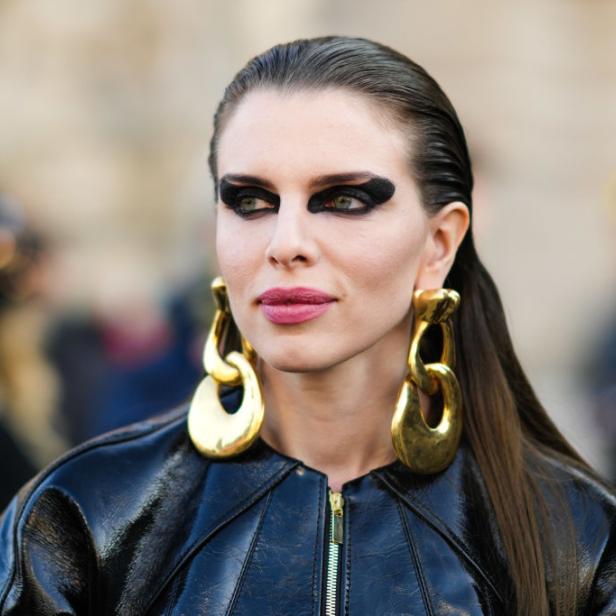Eine Frau mit starkem, schwarzem Augen-Make-up und großen, goldenen Ohrringen.