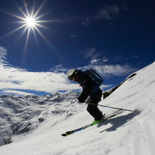 Ein Skifahrer fährt an einem sonnigen Tag einen schneebedeckten Hang hinunter.
