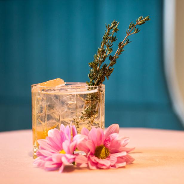 Ein Cocktail mit Eis, Thymian und rosa Blumen auf einem Tisch.