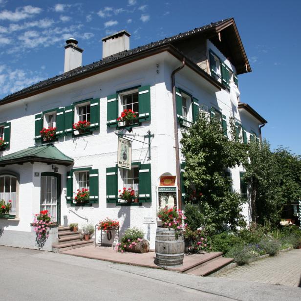 Das Gasthaus „Wirt am Gries“ mit grünen Fensterläden und Blumenkästen an einem sonnigen Tag.
