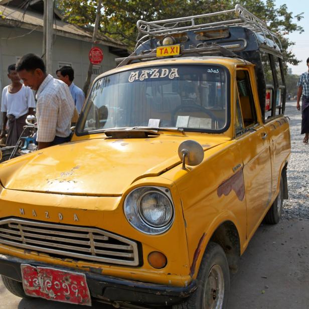 Ein gelbes Mazda-Taxi steht auf einer Straße in Myanmar.