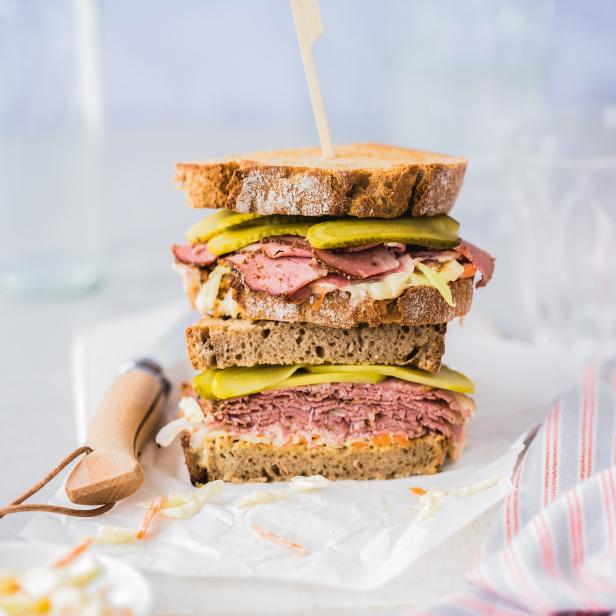 Ein hoch gestapeltes Sandwich mit Corned Beef, Sauerkraut und Gurken auf Roggenbrot.