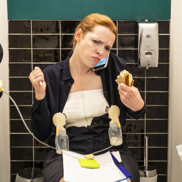 Eine Frau telefoniert, isst ein Sandwich und benutzt gleichzeitig eine Milchpumpe.