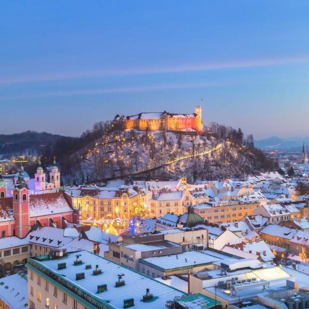 Winterliche Ansicht von Ljubljana mit der Burg auf einem Hügel, beleuchtet in der Dämmerung.