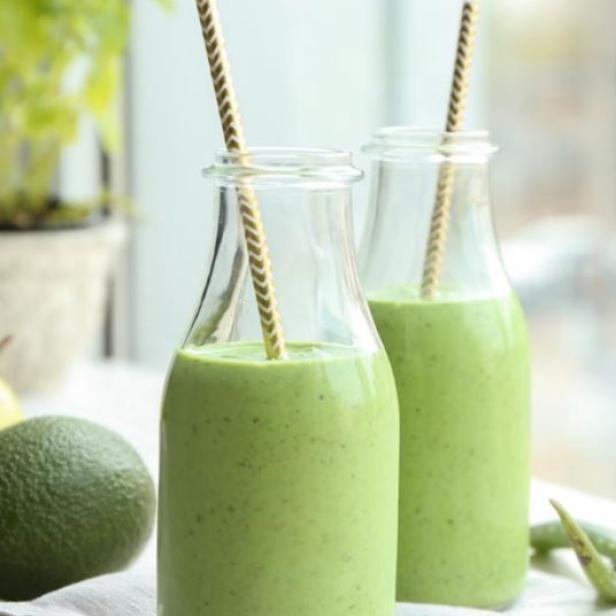 Zwei Flaschen mit grünem Smoothie und Papierstrohhalmen stehen auf einem Tisch.