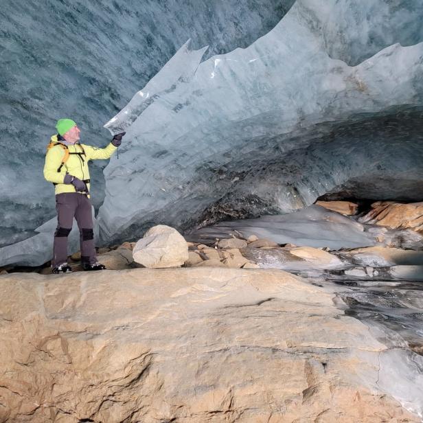 Ein Mann steht in einer Eishöhle und berührt eine Eisformation.