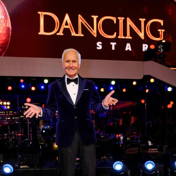Ein Mann in einem blauen Samtjackett und Fliege steht auf einer Bühne vor dem "Dancing Stars"-Logo.