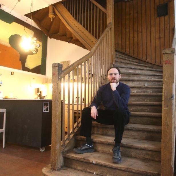 Ein Mann sitzt auf einer Holztreppe in einem hellen Raum.