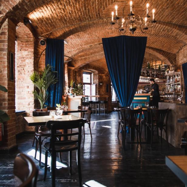 Innenansicht eines Restaurants mit Ziegelgewölbe und blauen Vorhängen.