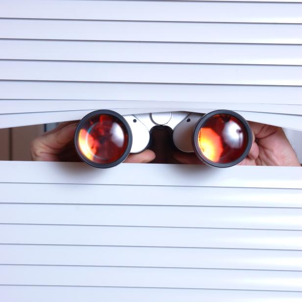Jemand schaut mit einem Fernglas durch die Jalousien.