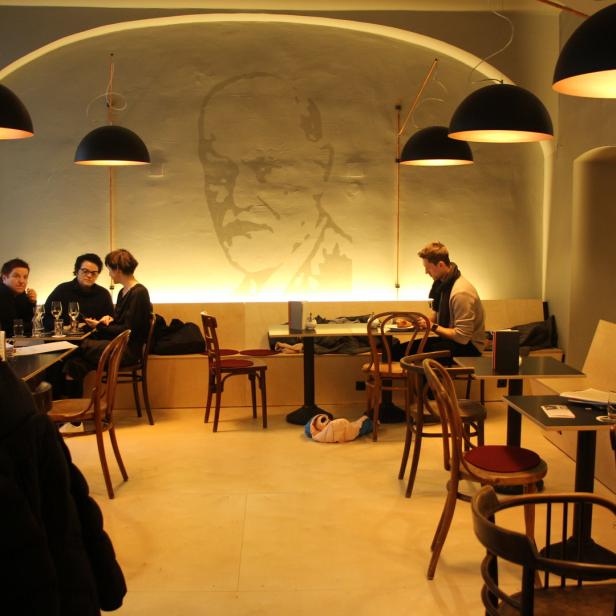 Mehrere Personen sitzen in einem Café unter großen, runden Lampen.