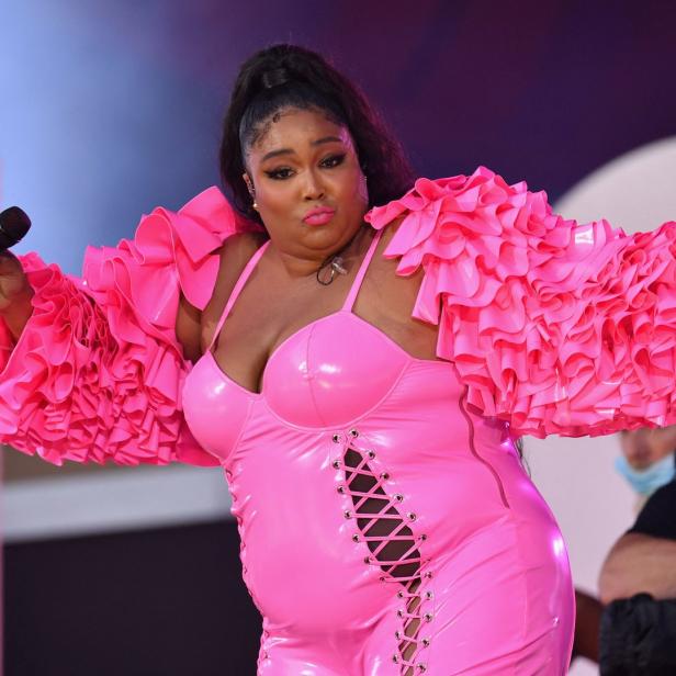 Lizzo tritt in einem pinkfarbenen Outfit mit Rüschenärmeln auf und hält ein Mikrofon.
