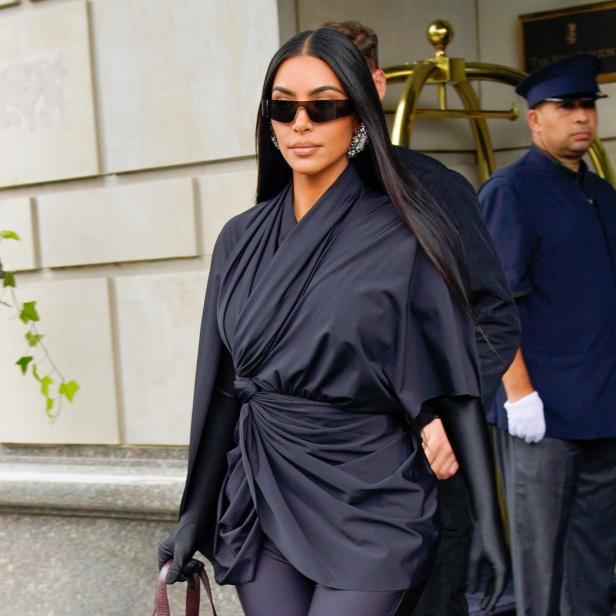 Kim Kardashian verlässt ein Gebäude in einem schwarzen Outfit und Sonnenbrille.