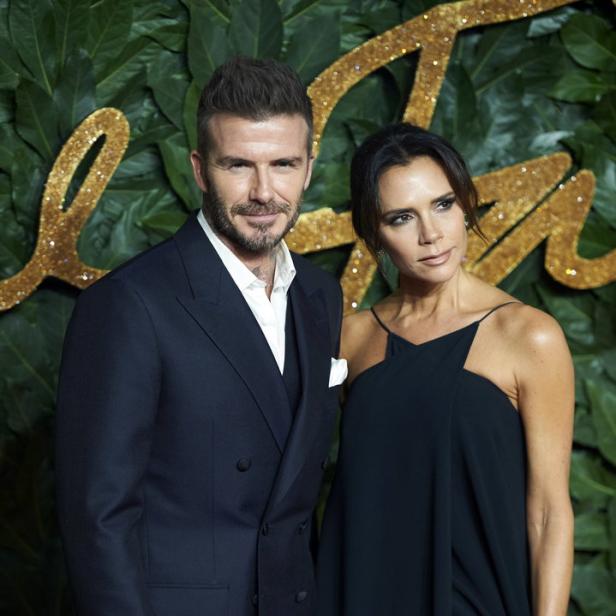 David und Victoria Beckham posieren auf einem Event vor einer Wand aus Blättern.