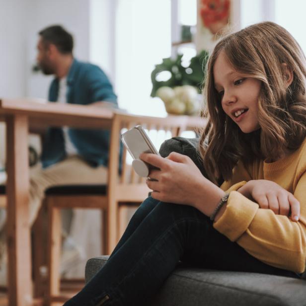 Ein Mädchen sitzt auf einem Sofa und schaut auf ihr Handy.