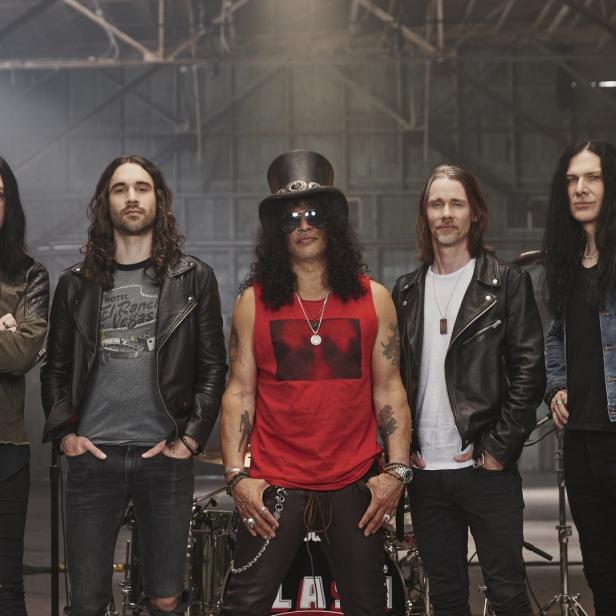 Die Rockband Slash posiert vor einem Schlagzeug in einer Lagerhalle.