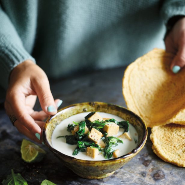 Eine Person hält eine Schüssel mit Spinat-Tofu-Suppe und Tortillas.
