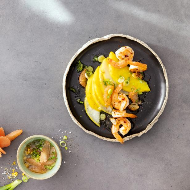 Ein Teller mit Mango, Garnelen und Frühlingszwiebeln auf einem grauen Tisch.