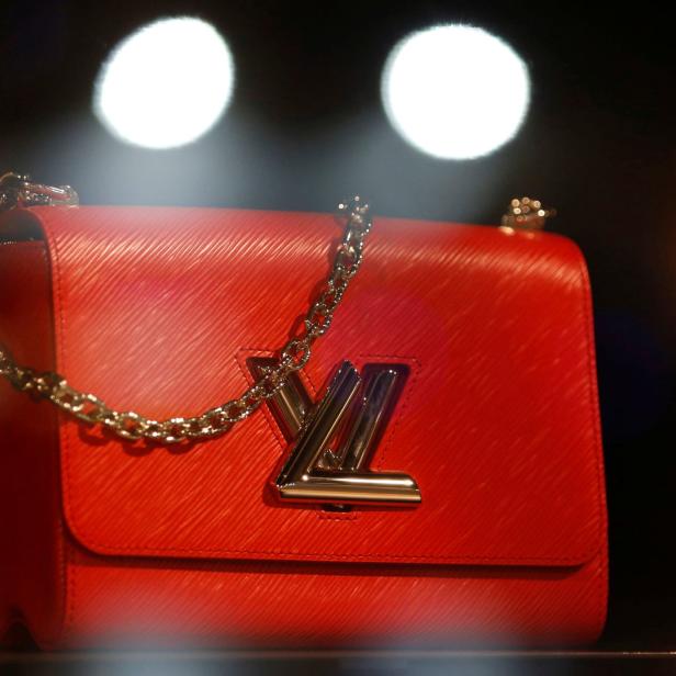 Eine rote Louis Vuitton Handtasche mit silberner Kette und Logo vor dunklem Hintergrund.