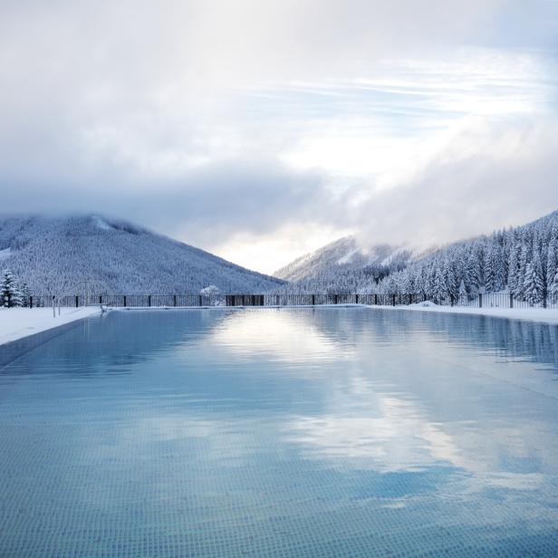 Ein Schwimmbecken spiegelt die schneebedeckten Berge und den bewölkten Himmel wider.