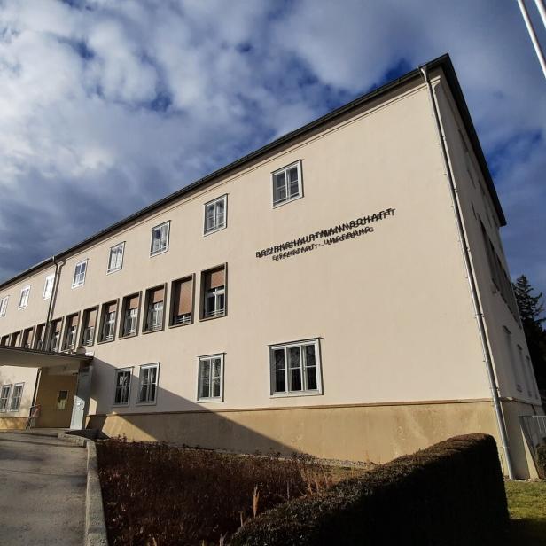 Ein langes, helles Verwaltungsgebäude mit mehreren Fenstern und einem Schriftzug an der Fassade bei bewölktem Himmel.