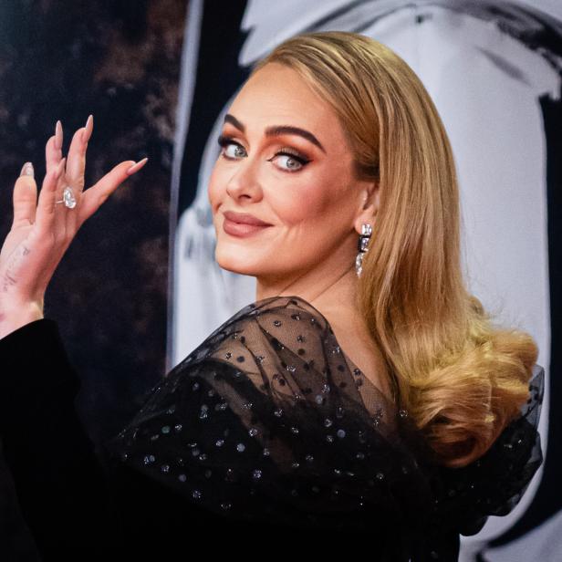 Adele blickt über die Schulter und zeigt ihren Diamantring.