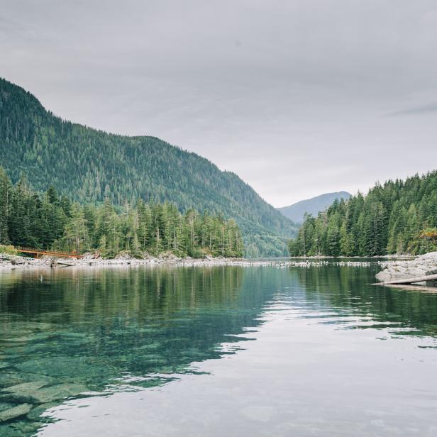 Klares Wasser spiegelt die bewaldeten Berge an einem ruhigen Tag wider.