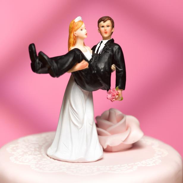 Ein Bräutigam trägt eine Braut als Tortenaufsatz auf einer Hochzeitstorte.