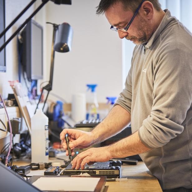 Ein Mann mit Brille repariert einen Laptop mit einem Schraubendreher.
