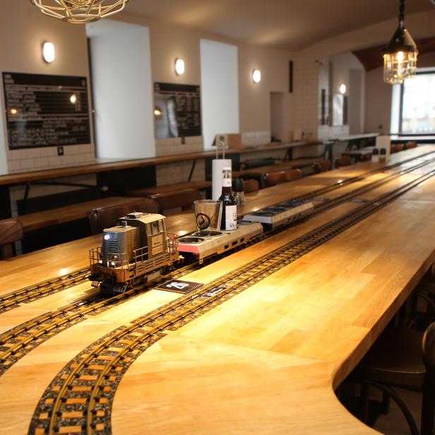 Ein Miniaturzug transportiert Getränke auf einer langen Holztischplatte in einem Restaurant.