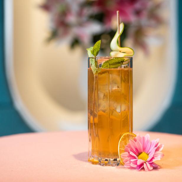 Ein erfrischender Cocktail mit Eis, Minze und Gurke auf einem rosa Tisch, dekoriert mit einer rosa Blume.