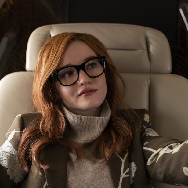 Eine Frau mit roten Haaren und Brille sitzt in einem Privatjet und macht ein Selfie.