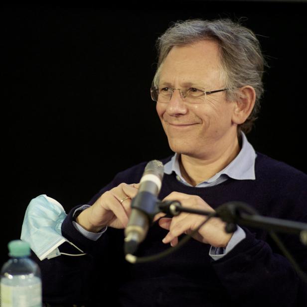 Ein Mann mit Brille lächelt und hält ein Mikrofon in den Händen.