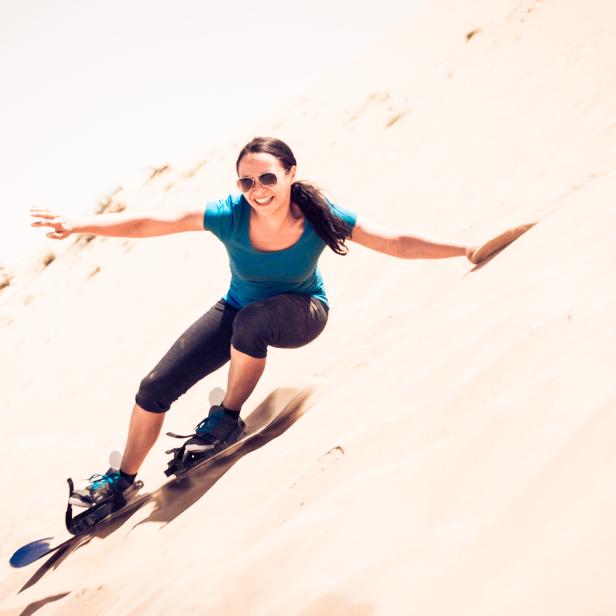 Eine Frau fährt mit einem Sandboard eine Düne hinunter.