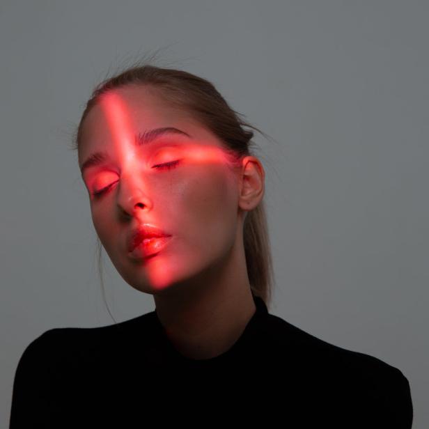 Das Gesicht einer Frau wird von einem roten Lichtkreuz beleuchtet.