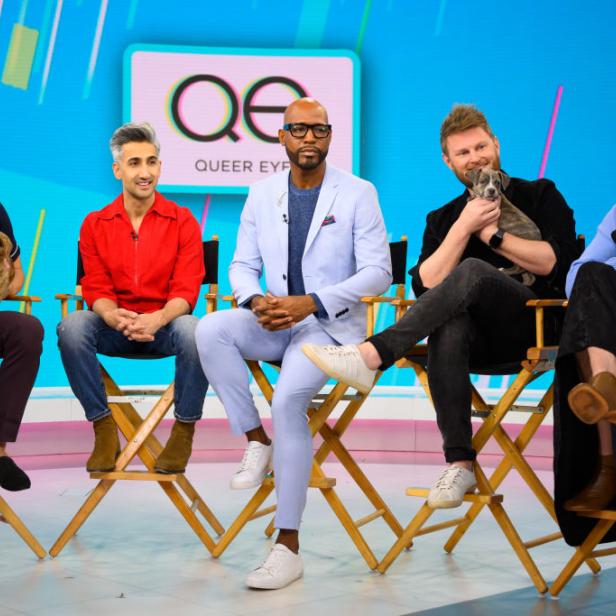 Die Besetzung von „Queer Eye“ sitzt mit Welpen auf Stühlen vor einem Queer Eye-Logo.