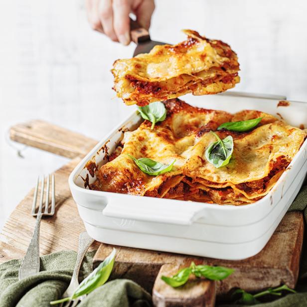 Eine Portion Lasagne wird aus einer Auflaufform gehoben.