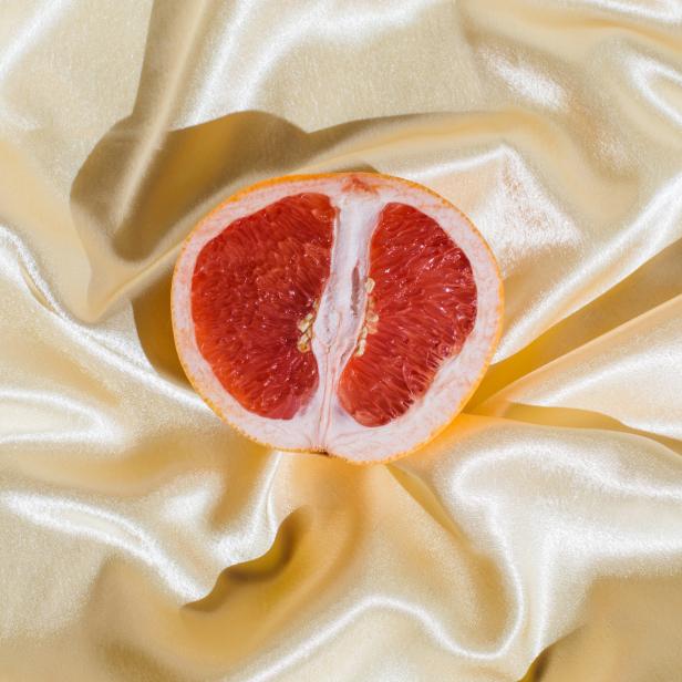 Eine halbe Grapefruit liegt auf einem drapierten, goldenen Stoff.