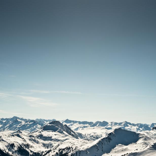 Eine weite, schneebedeckte Berglandschaft unter einem hellblauen Himmel.