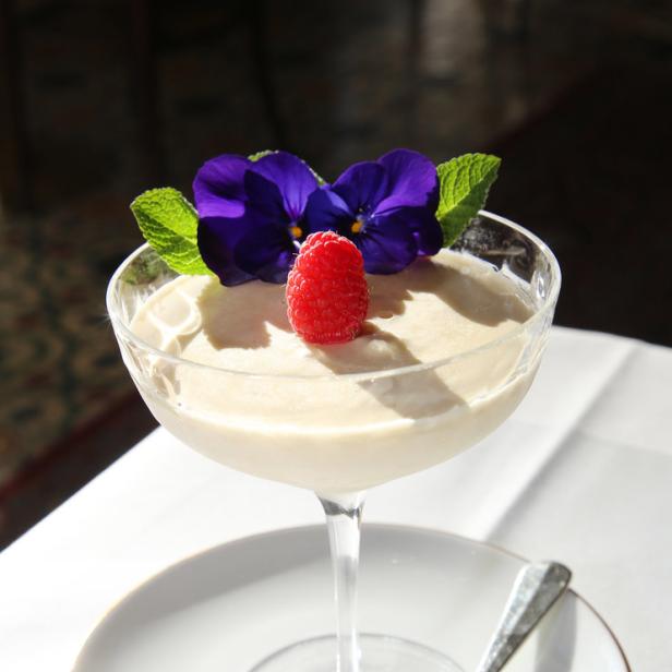 Ein Dessert in einem Glas, garniert mit einer Himbeere, Veilchen und Minze.