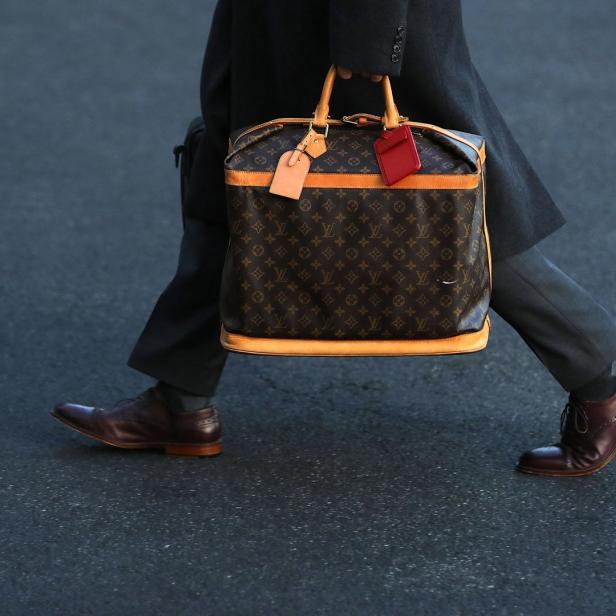 Eine Person trägt eine Louis-Vuitton-Tasche und braune Lederschuhe.
