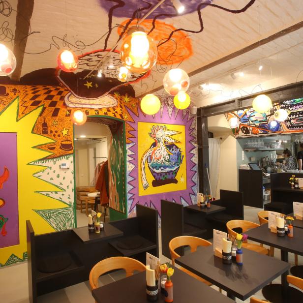 Innenansicht eines Restaurants mit farbenfrohen Wandmalereien und Tischen.