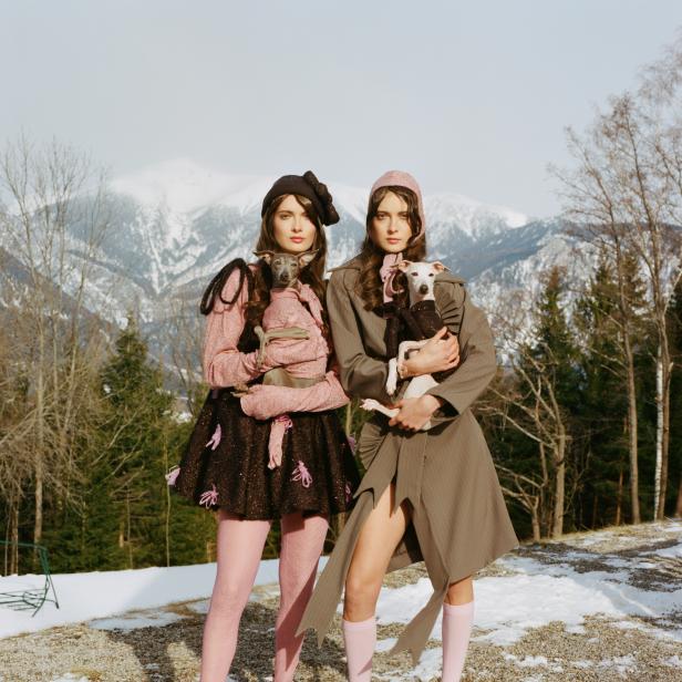 Zwei Frauen mit Hunden posieren vor einer verschneiten Berglandschaft.