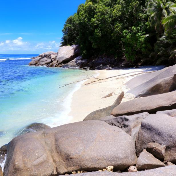 Ein Strand mit großen Felsen im Vordergrund und türkisfarbenem Wasser im Hintergrund.